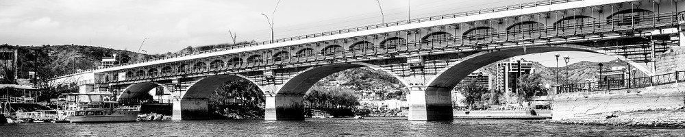 Schwarzweissaufnahme mit Eisenbahnbrücke, die über einen breiten Fluss führt